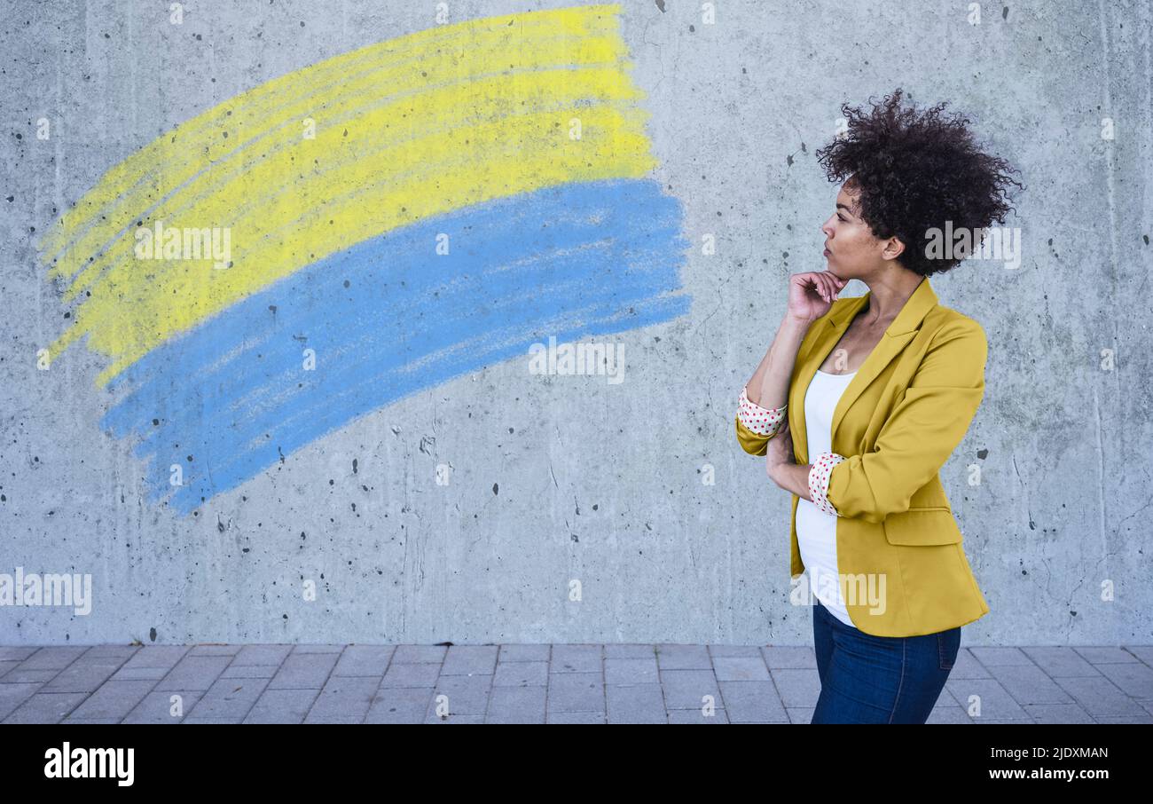 Giovane donna che guarda la bandiera ucraina dipinta sul muro Foto Stock