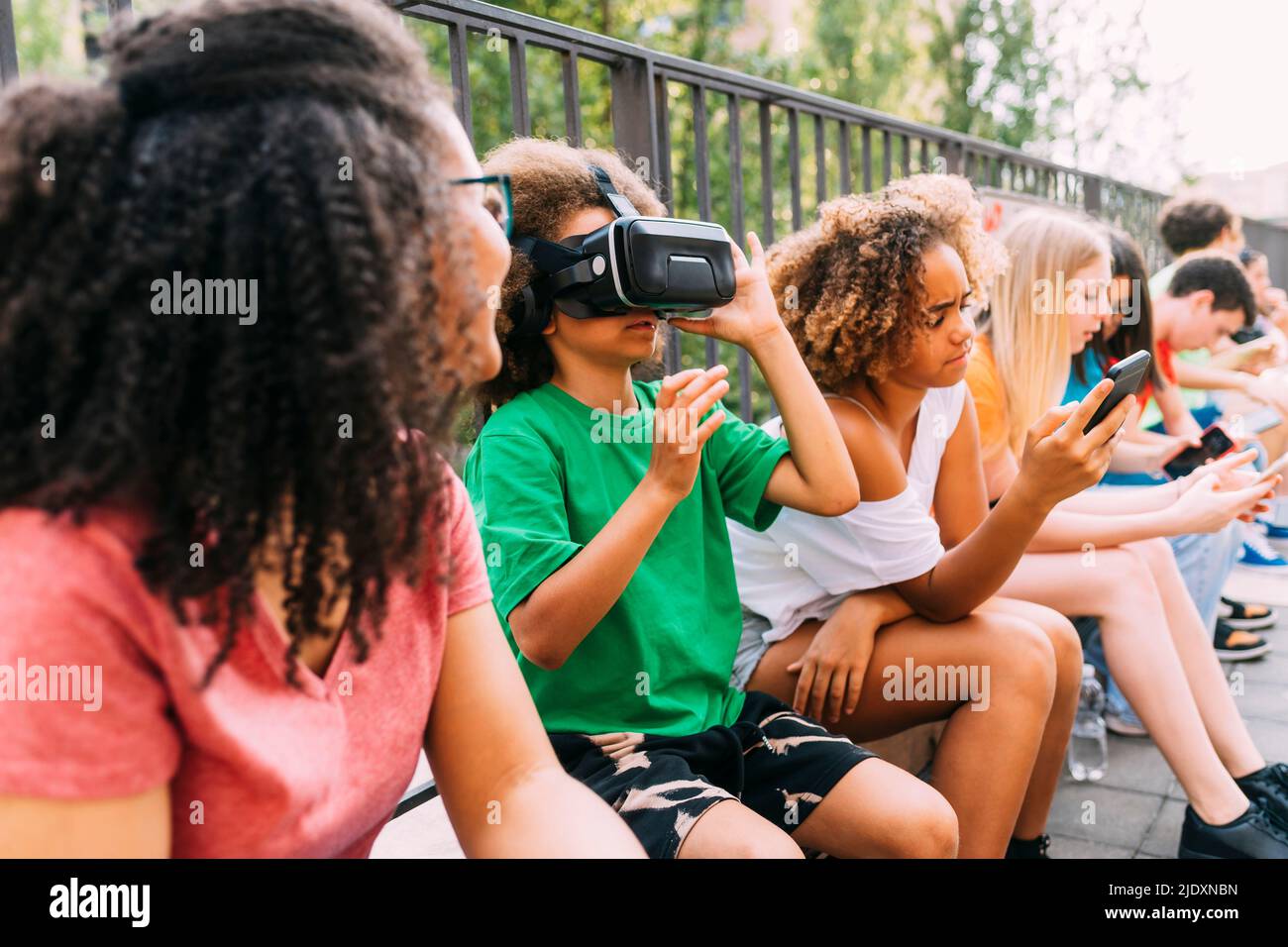Ragazzo che indossa simulatore di realtà virtuale seduto con gli amici utilizzando lo smartphone Foto Stock