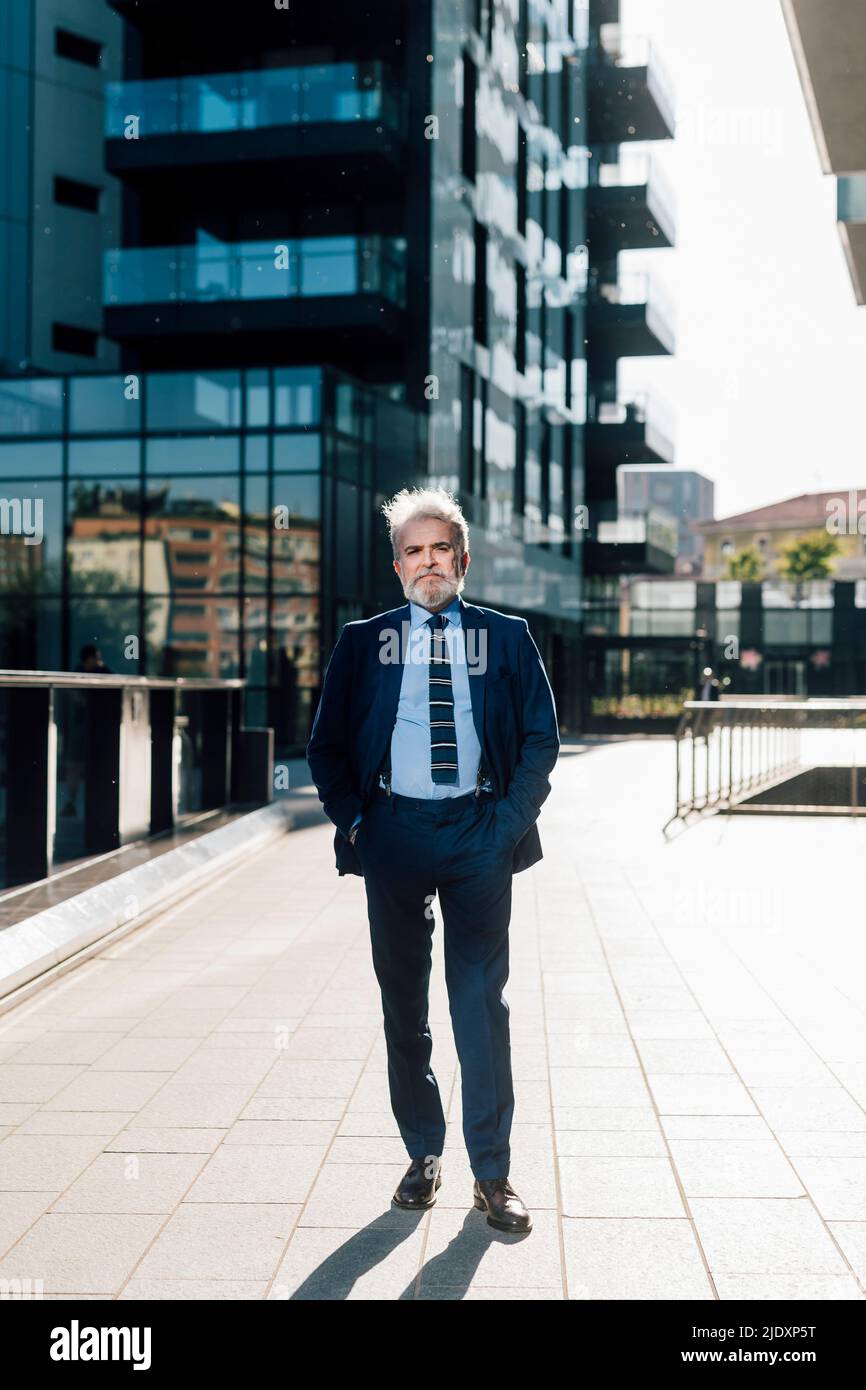 Uomo d'affari anziano che posa con le mani nelle tasche fuori dell'edificio dell'ufficio Foto Stock