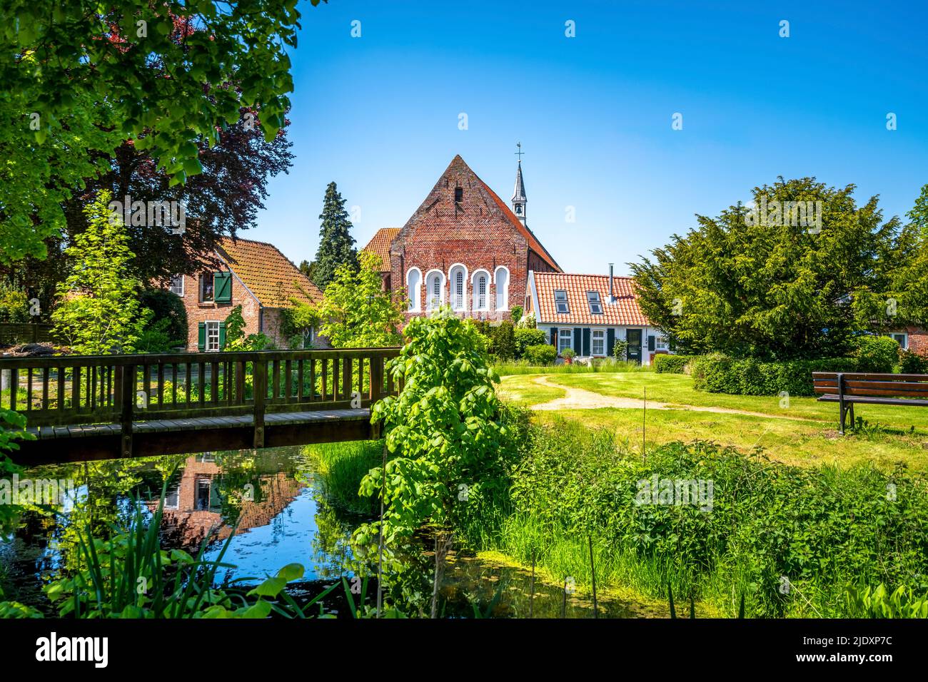 Germania, bassa Sassonia, Krummhorn, piccolo ponte sull'acqua in piedi con la chiesa di Loquard sullo sfondo Foto Stock