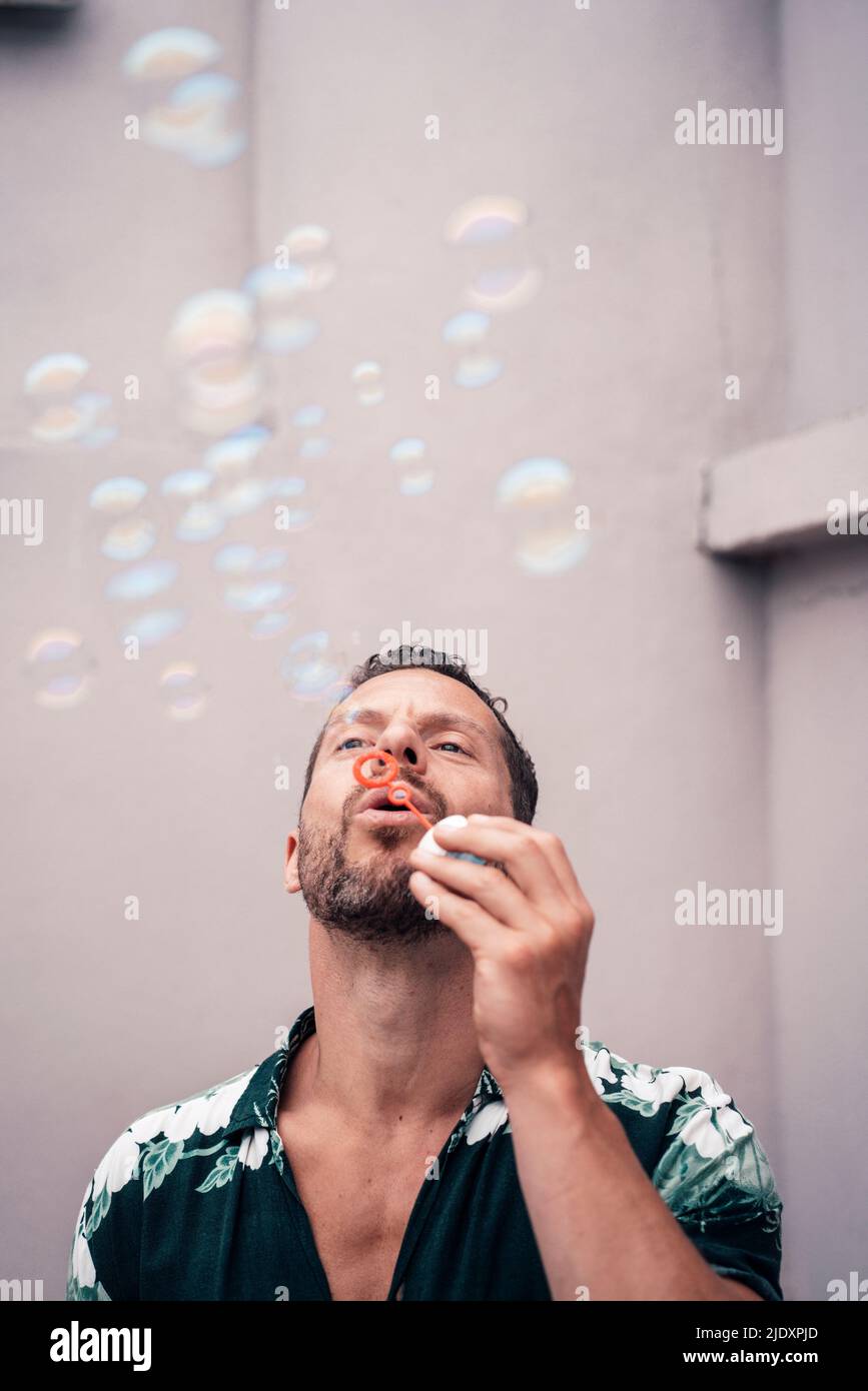 Uomo maturo che soffia bolle davanti al muro Foto Stock