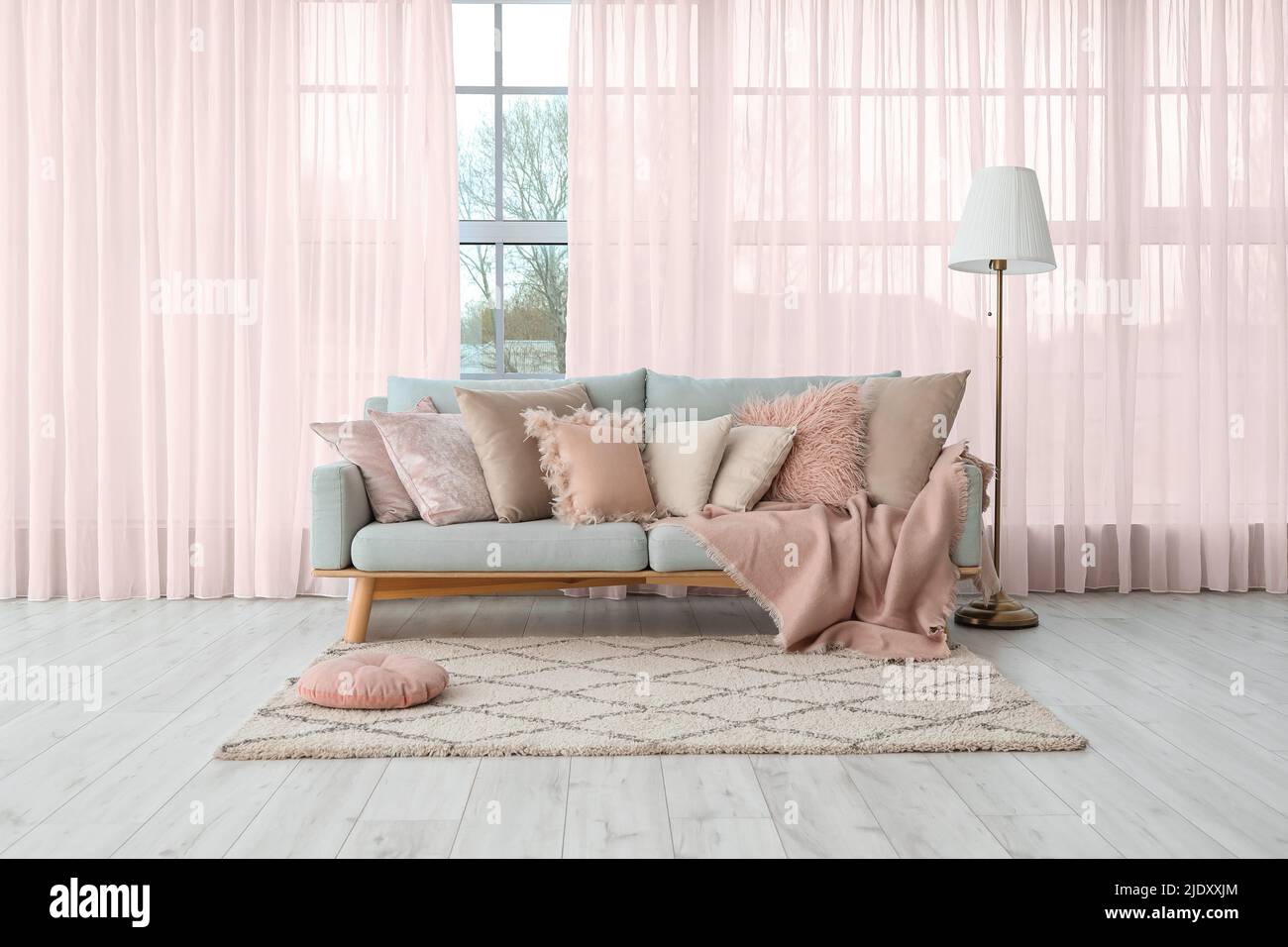 Divano grigio con morbidi cuscini e lampada vicino alla grande finestra con  tende rosa nel soggiorno Foto stock - Alamy