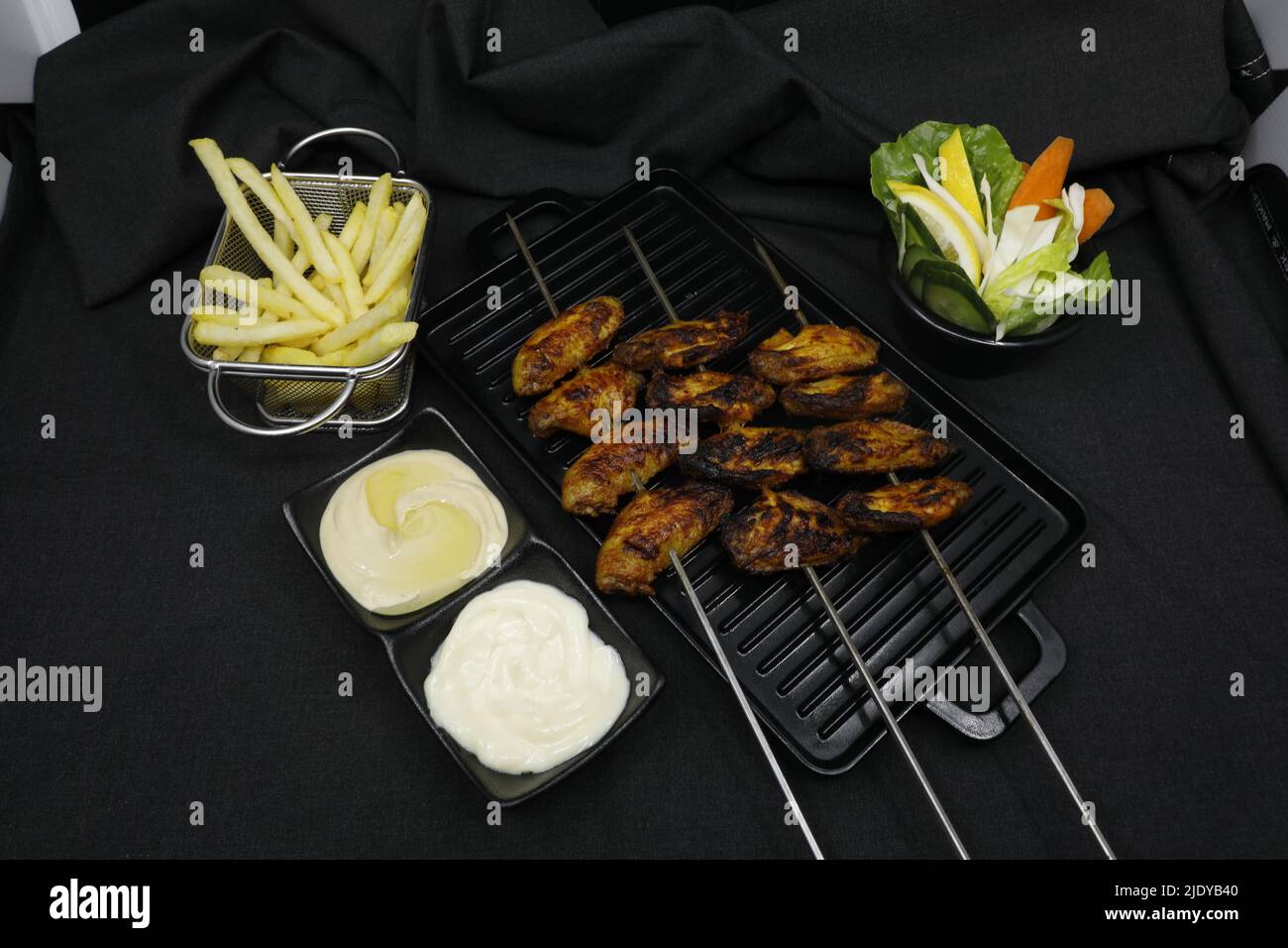 ali di pollo grigliate con patatine fritte e insalata di salsa su sfondo nero Foto Stock