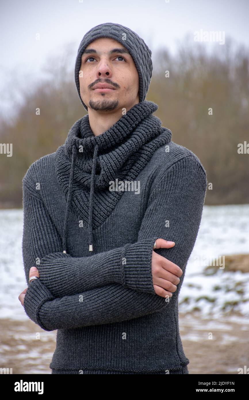 Un giovane si alza con le braccia incrociate da un lago. Guarda in su pensieroso. Foto Stock