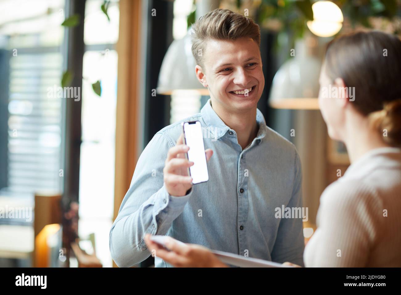 Un bel manager giovane in maglietta casual che mostra una comoda app mobile ai colleghi mentre discutono di promozione aziendale Foto Stock