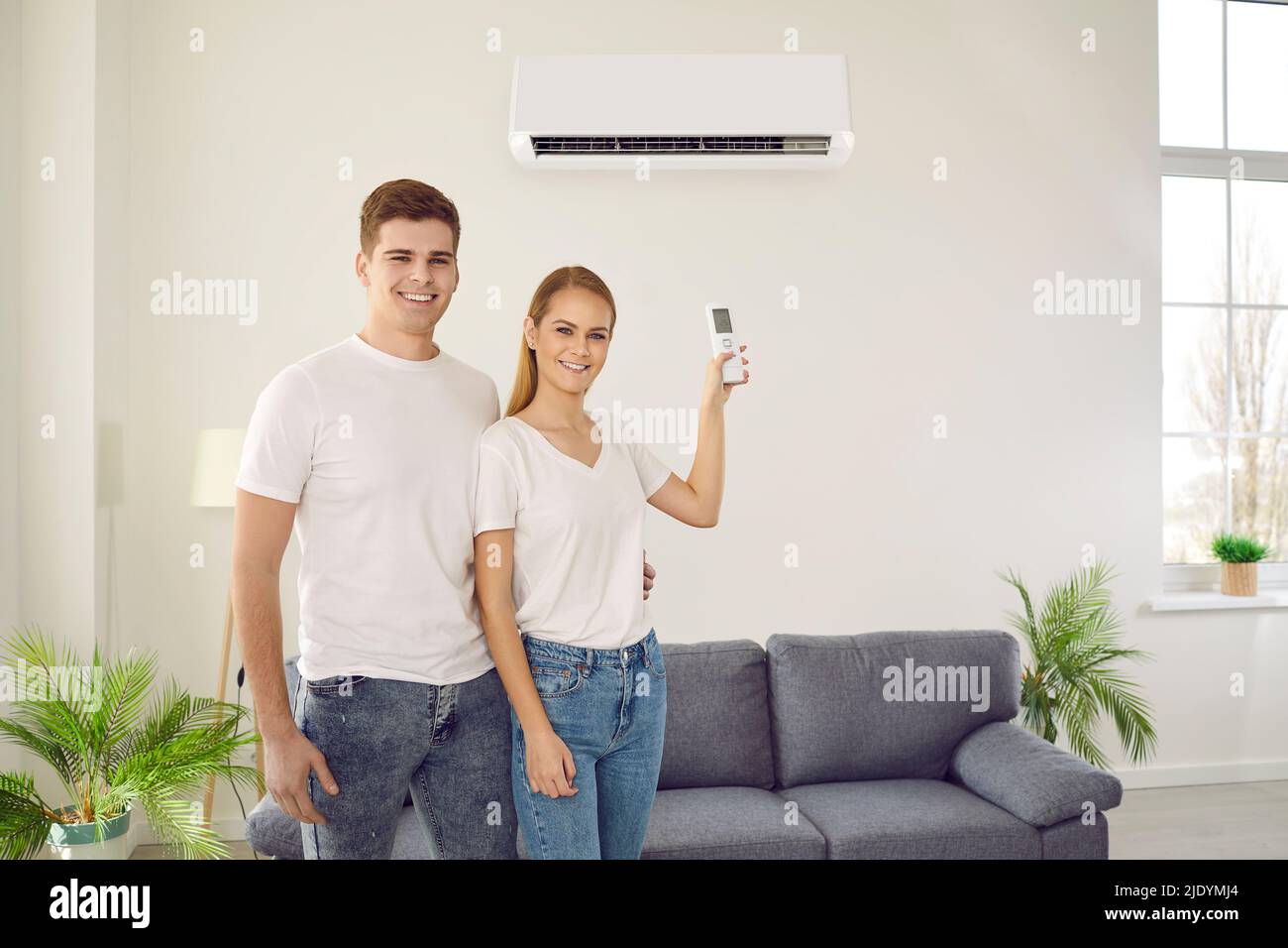 Coppia felice godendo usando il condizionatore d'aria appena installato nel soggiorno della loro casa. Foto Stock