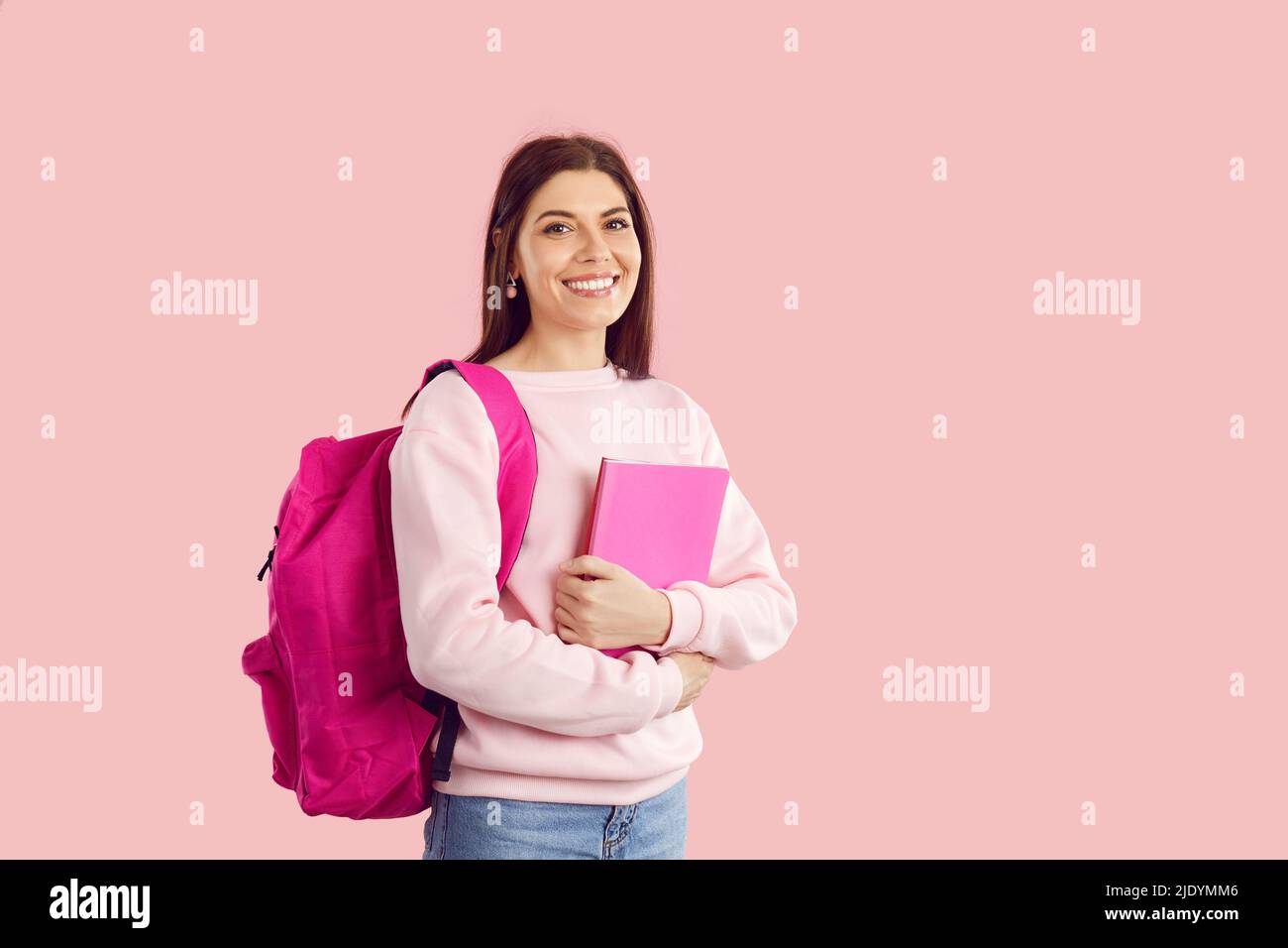 Felice università studentessa ragazza con libri e zaino in piedi isolato su sfondo rosa Foto Stock