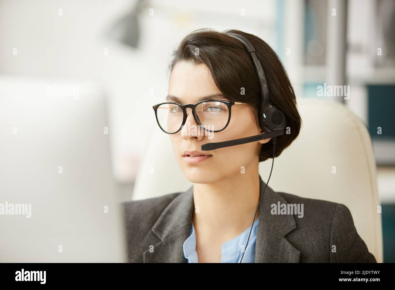 Serio e pensivo attraente hotline specialista in cuffie e auricolari che utilizzano l'app per videoconferenze, rispondendo alle domande degli utenti software Foto Stock