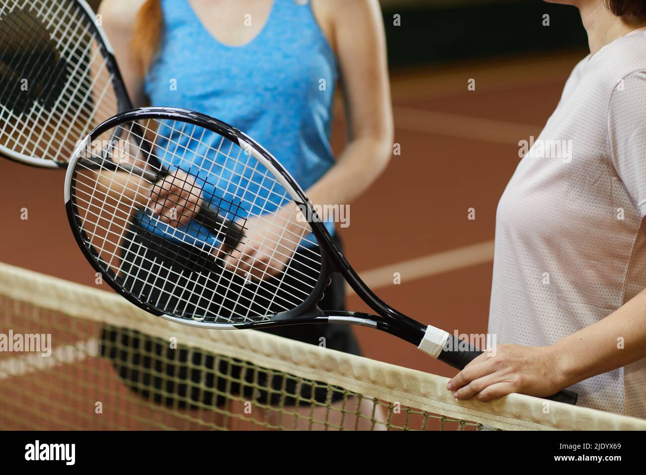 Primo piano di irriconoscibili giocatori di tennis femminile in piedi alla rete e tenere racquets personali durante la discussione di gioco Foto Stock