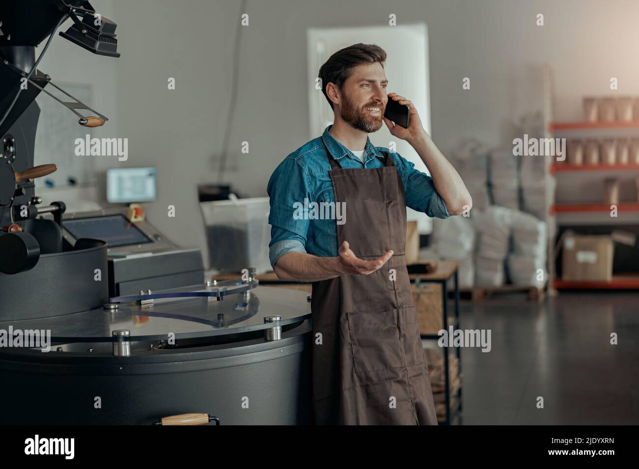 Il proprietario di affari che parla il telefono sullo sfondo della macchina da caffè tostatura Foto Stock