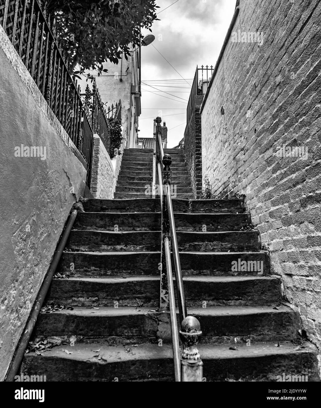 I gradini vecchi e usurati conducono verso l'alto. Un muro di mattoni dipinto è un lato e un bianco uno sull'altro. Un corrimano si trova al centro e un albero si inclina su t Foto Stock