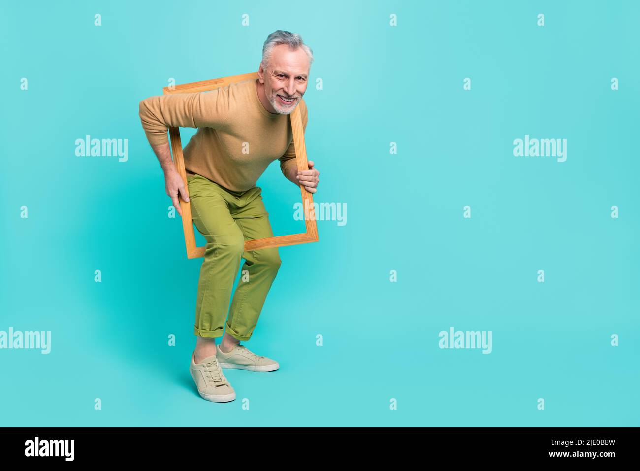 Ritratto a grandezza naturale di un uomo allegro e allegro hanno uno sguardo divertente attraverso la cornice di legno isolato su sfondo di colore turchese Foto Stock