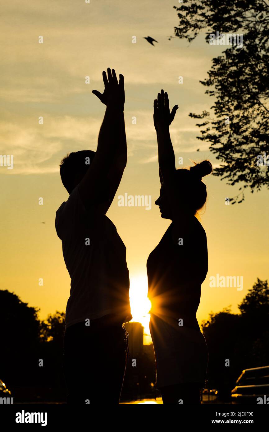 Giovane coppia che si esercita sulla strada in città da sotto vista, sfondo tramonto. Silhouette oscurate di uomo e donna che si allenano in piedi e in piedi Foto Stock