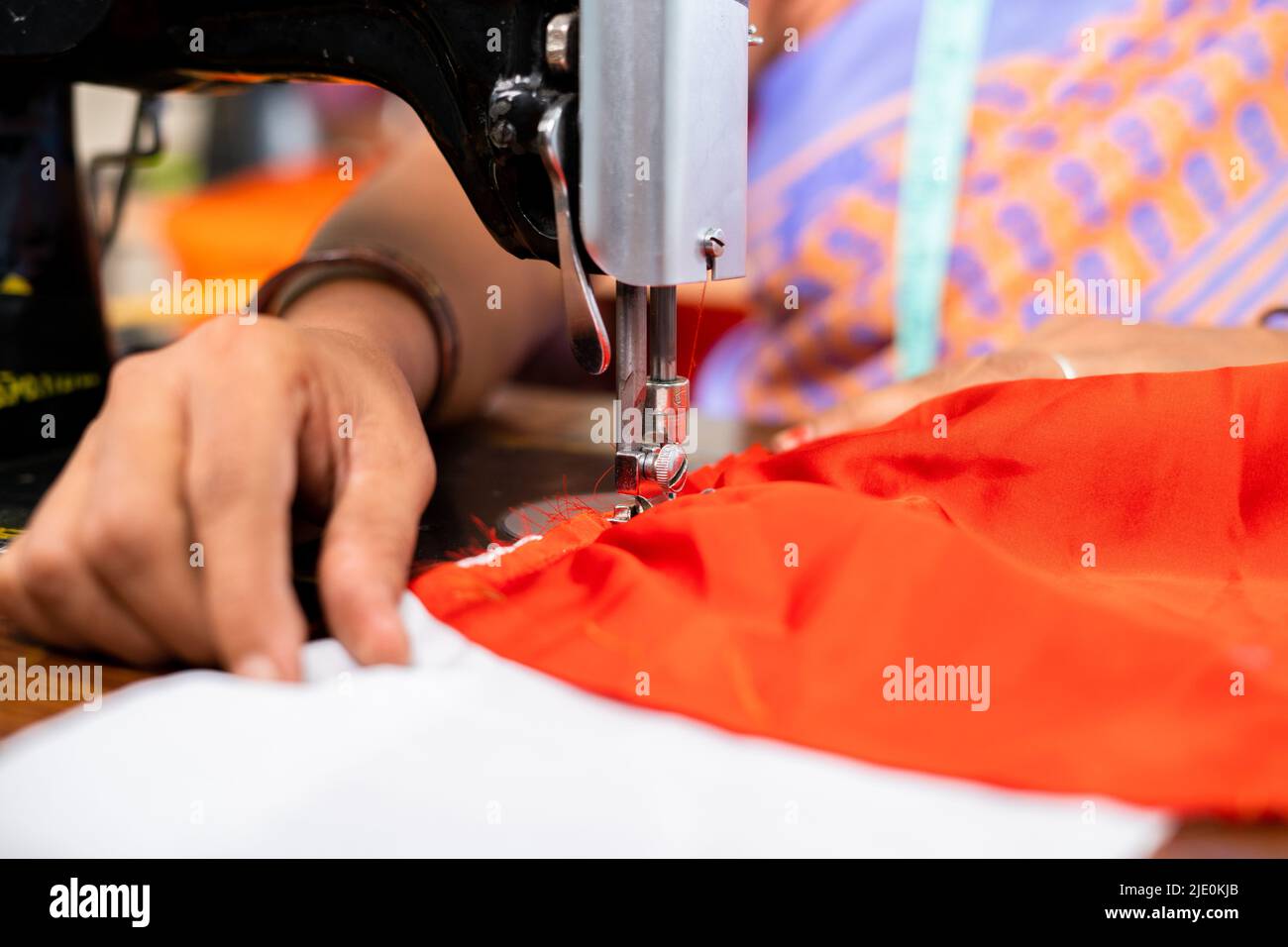 Primo piano, mani di donna indiana a capi di abbigliamento occupato sartoria o cuciture utilizzando la macchina da cucire - concetto di lavoro, competenza e piccola impresa domestica. Foto Stock