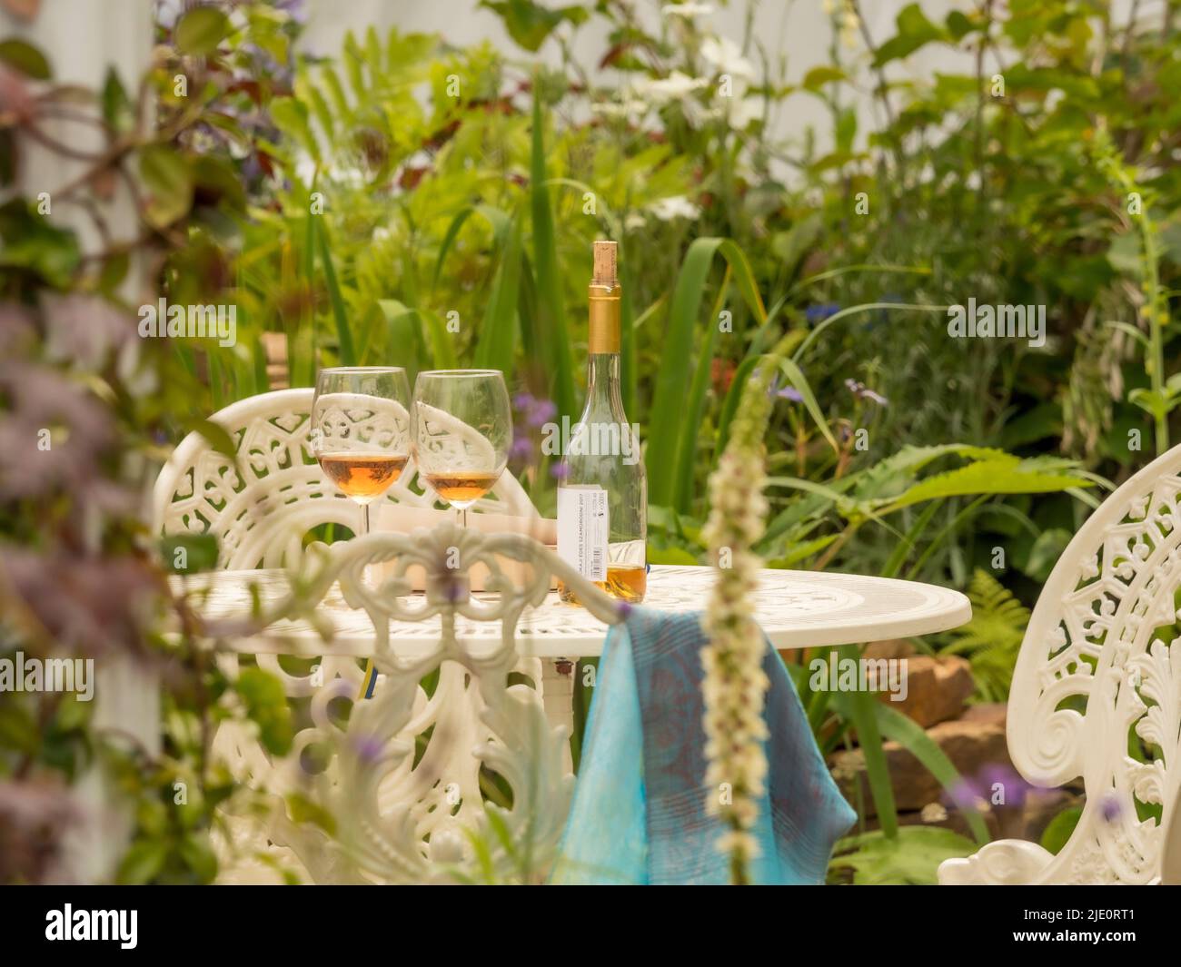 Bottiglia di vino con 2 bicchieri e libro cartaceo su un tavolo da giardino in ghisa bianca. Foto Stock