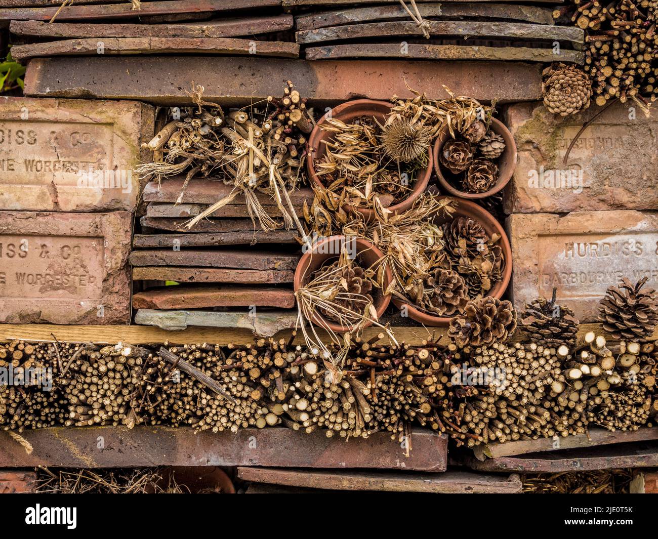 Bug hotel composto da mattoni impilati, tegole, pentole e ramoscelli di piante, in un giardino britannico. Foto Stock