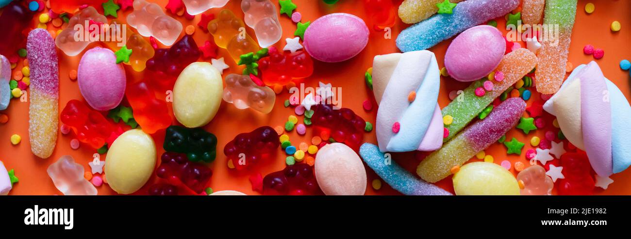 Vista dall'alto di dolci e caramelle in gelatina assortiti su sfondo arancione, striscione Foto Stock
