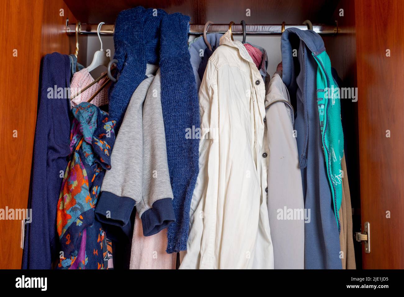 armadio aperto con vestiti su appendiabiti e disordine in cassetti