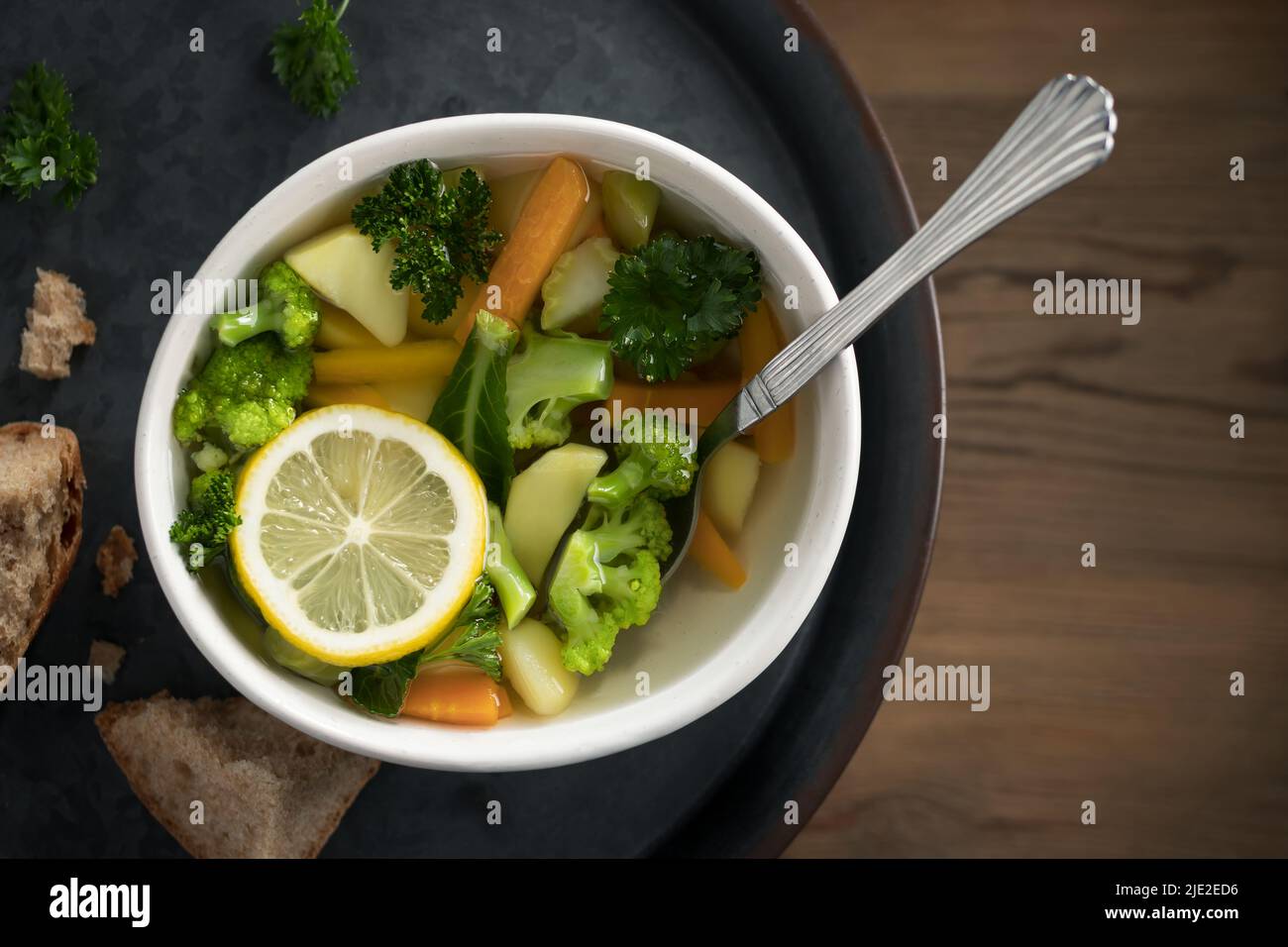 Zuppa vegetariana di verdure con carote, broccoli e prezzemolo in un recipiente leggero su un vassoio di metallo su un tavolo di legno. Foto Stock