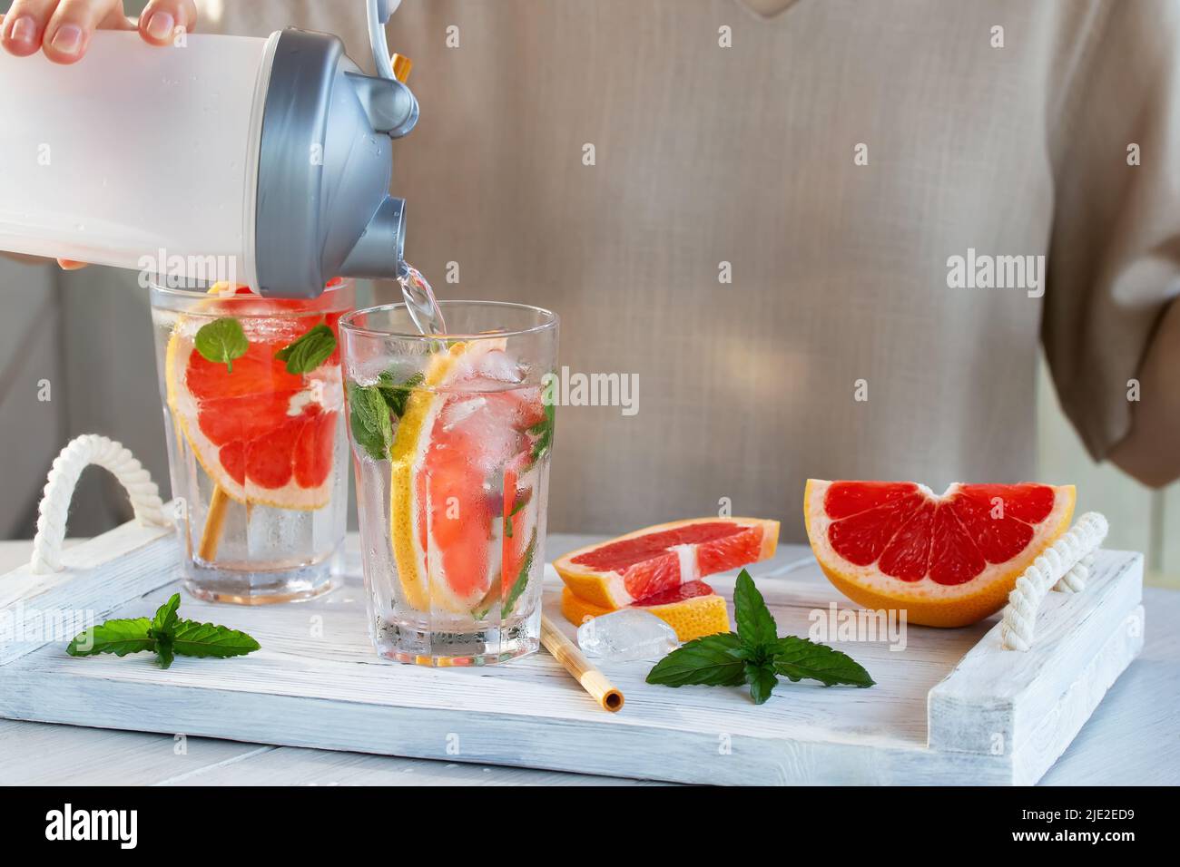 Ragazza cucina estate rinfrescante cocktail di frutta con fette di pompelmo e menta. Foto Stock