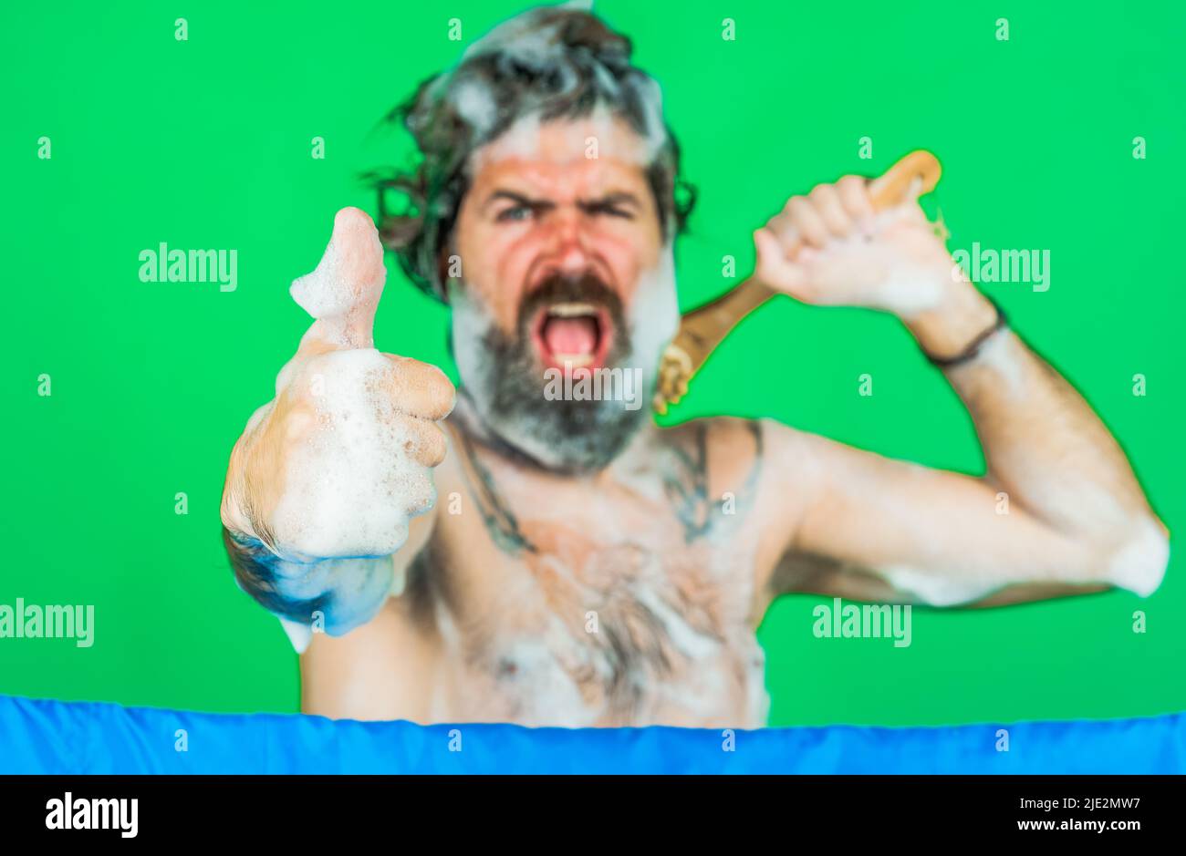 L'uomo bearded imbevuto con i lavaggi della schiuma nella doccia mostra il pollice su il gesto. Lavaggio del corpo. Cura dei capelli. Centro benessere. Foto Stock