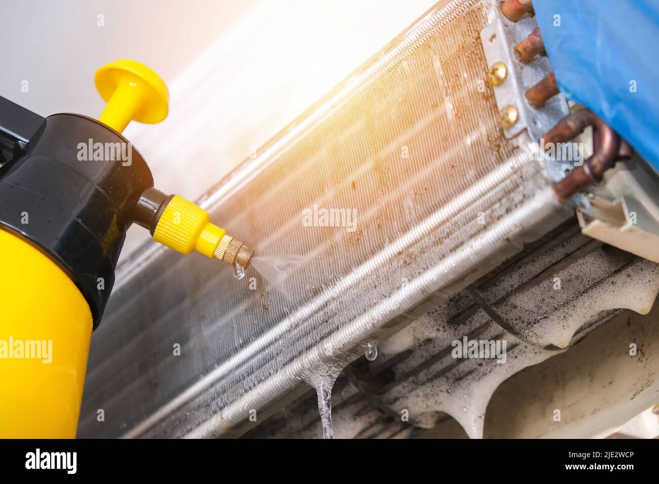 Un uomo lava via una schiuma speciale per pulire i condizionatori d'aria con un getto d'acqua sotto pressione. Manutenzione del sistema divisa. Foto Stock