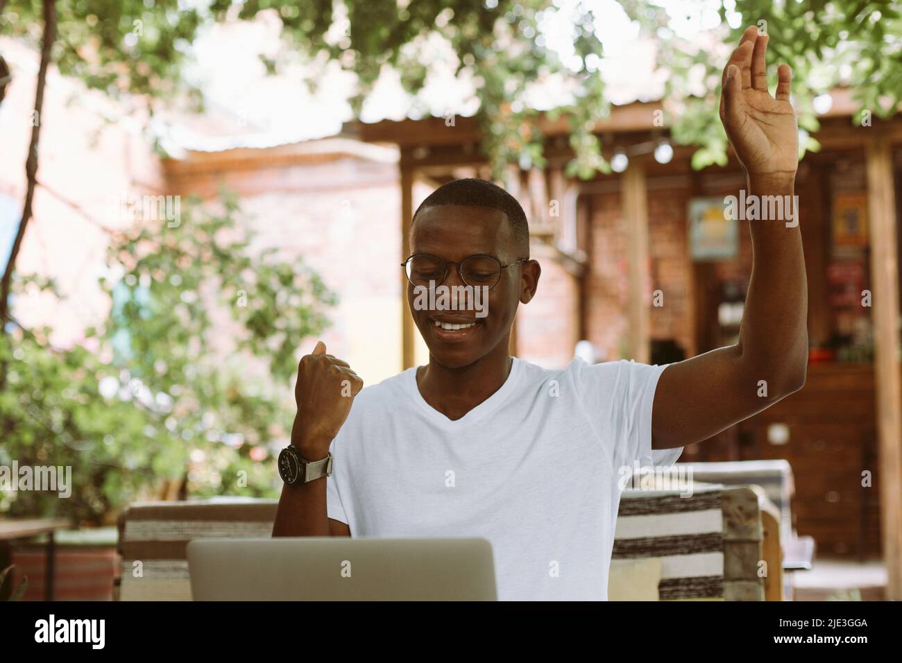 felice e ridendo uomo d'affari multirazziale in occhiali che lavorano su un portatile, sollevando braccio. Videochiamata, riunione online Foto Stock