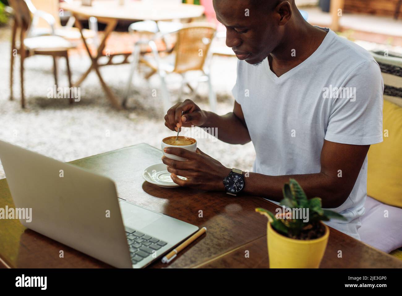 Un uomo d'affari multirazziale di successo, un freelance che beve caffè e lavora online utilizzando il laptop in un bar all'aperto. Fine settimana Foto Stock