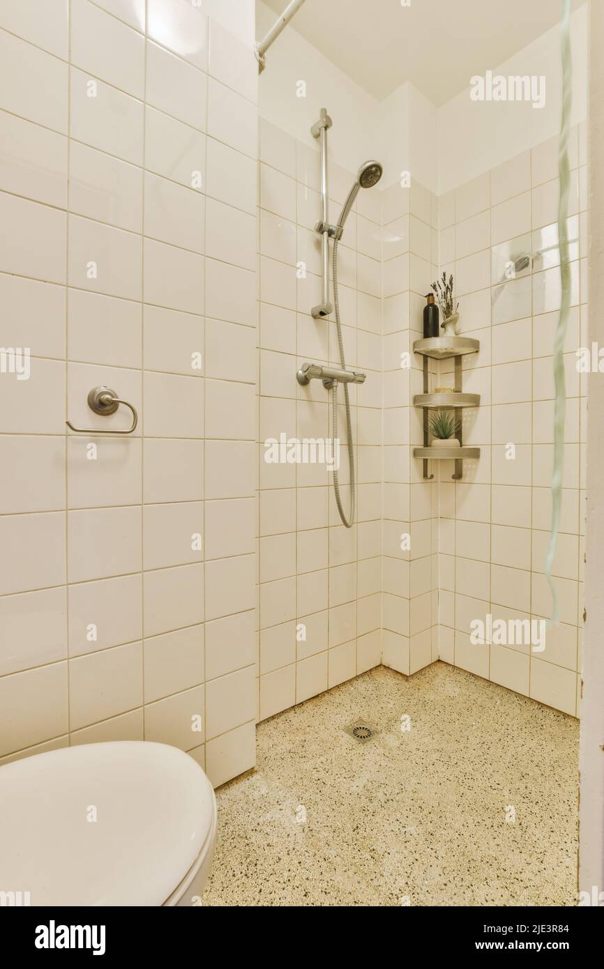 Rubinetti doccia attaccati ad una parete piastrellata bianca con mensole per articoli da bagno in un bagno a casa Foto Stock