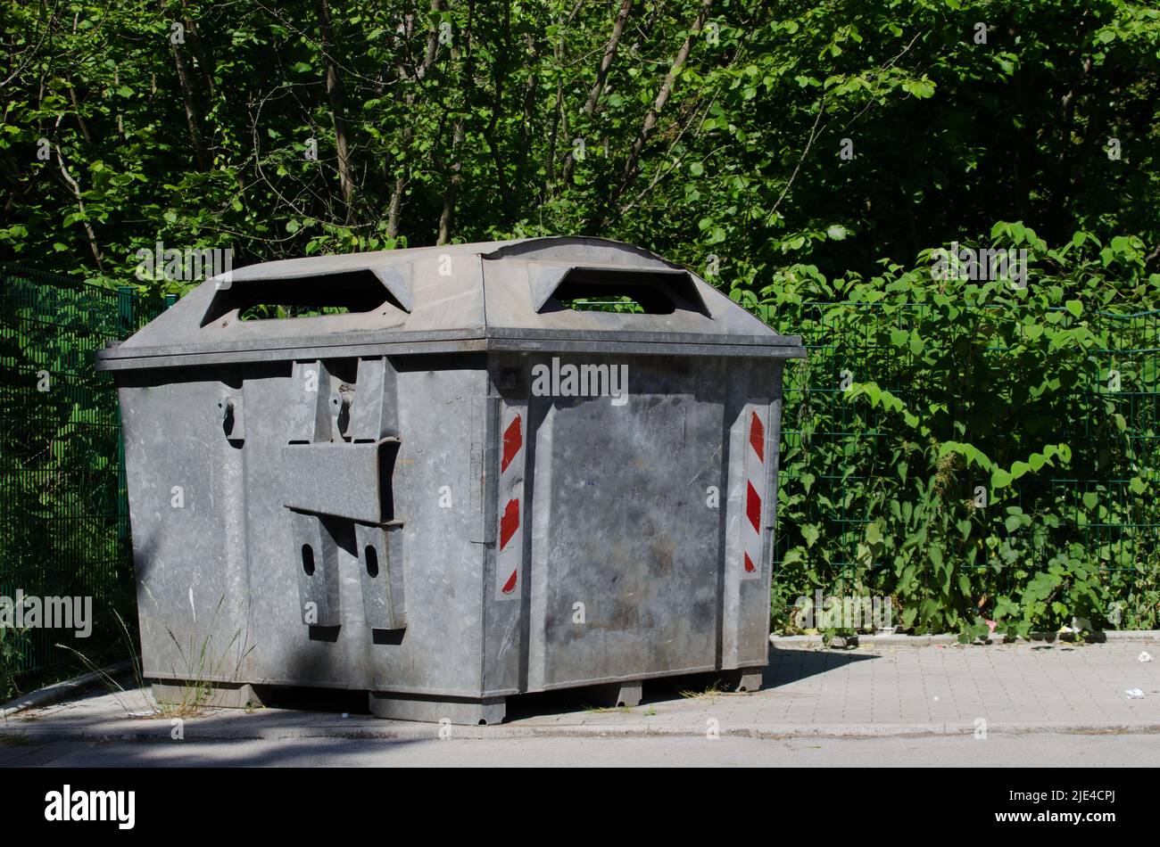 punto di raccolta del riciclaggio della carta / banca della carta vuota / grande dumpster fatto di acciaio con i riflettori in piedi beneith una strada con gli alberi nella parte posteriore Foto Stock