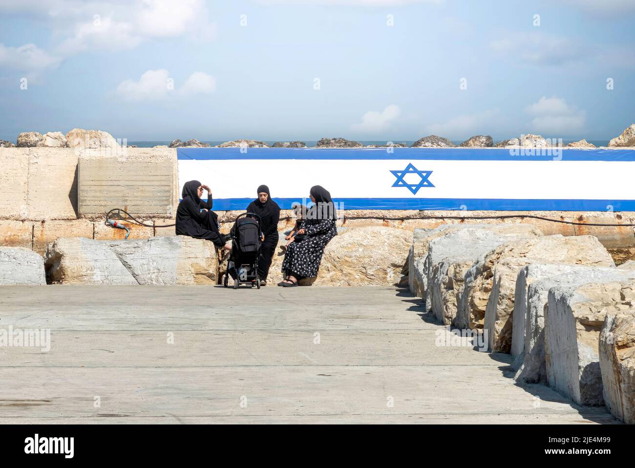 Donne arabe con chador, seduti nel porto di Jaffa vecchia con la bandiera israeliana sullo sfondo. Il concetto di pace. Foto di alta qualità Foto Stock