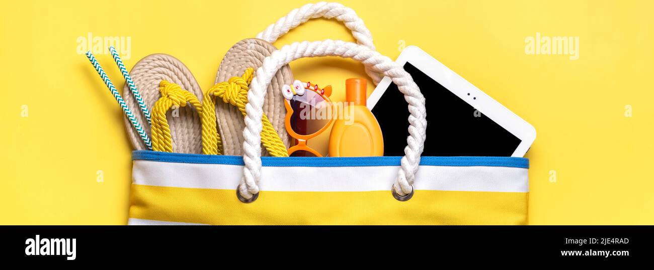 Accessori per il nuoto - borsa da spiaggia alla moda con strisce, occhiali neri, tavoletta bianca, foglia di palma, flop giallo su sfondo giallo Flat lay Top view Estate, viaggio, vacanza concept. Foto Stock