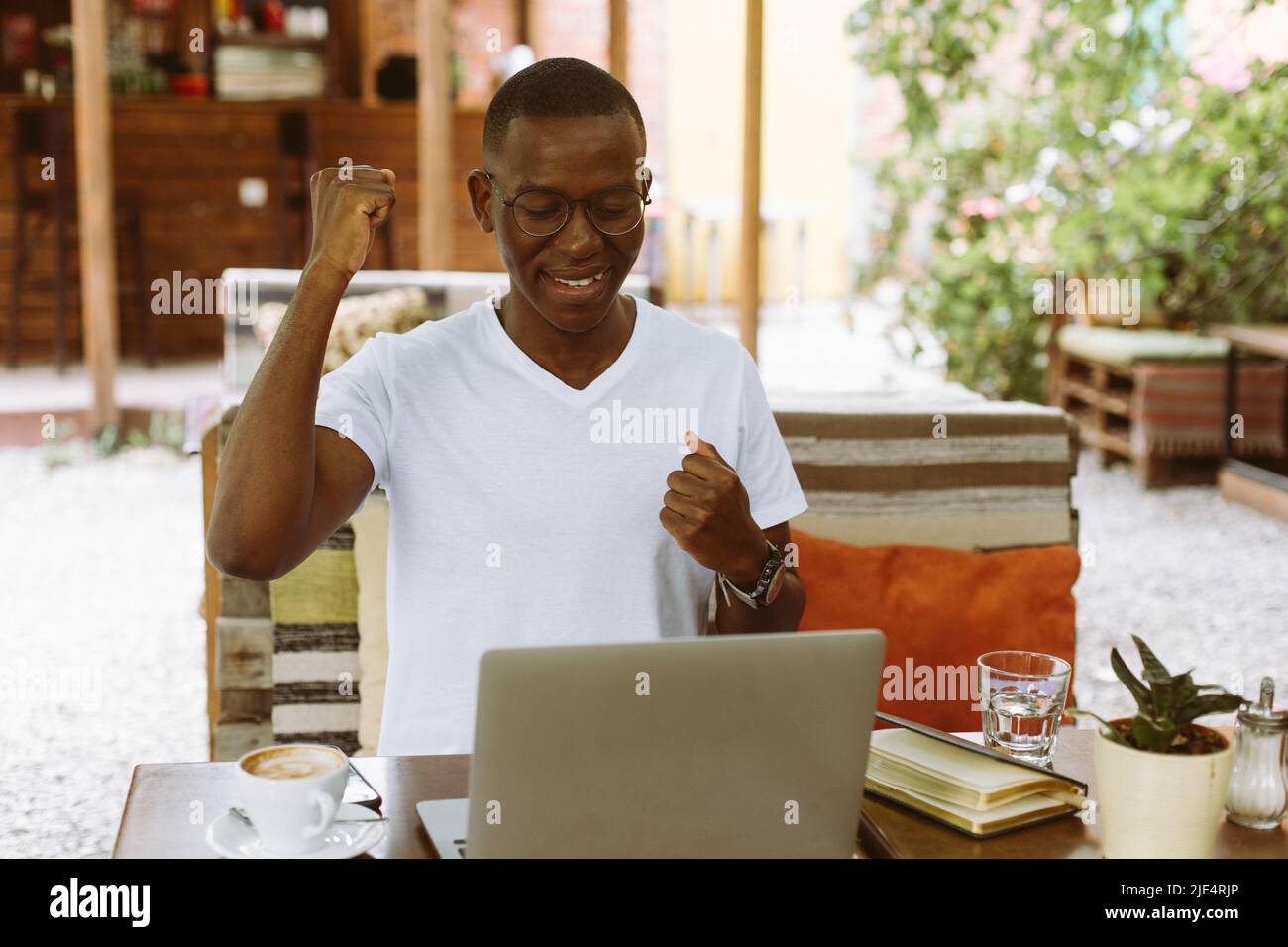 felice e ridendo uomo d'affari multirazziale in occhiali che lavorano su un portatile, sollevando braccio. Videochiamata, riunione online Foto Stock