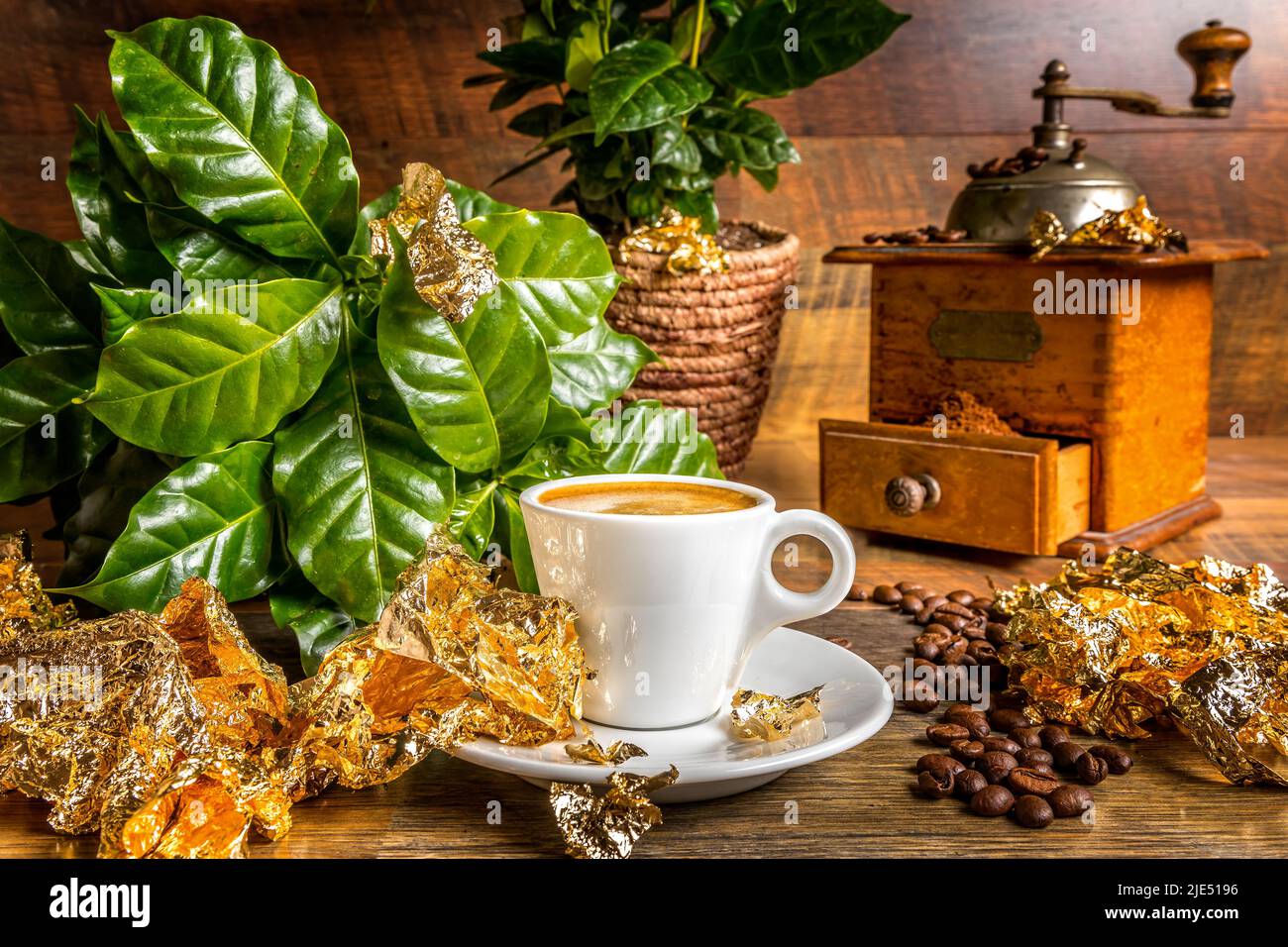 Caffè fresco, l'oro fluido. Una tazza con espresso appena fatto tra un vecchio macinacaffè e piante di caffè e foglie dorate Foto Stock