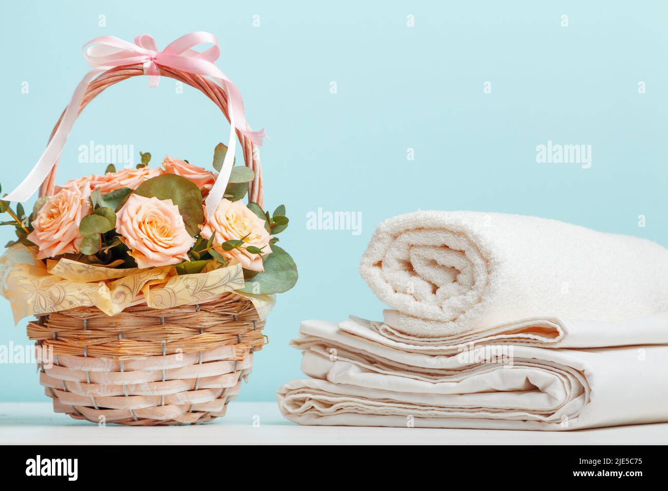 Lenzuola bianche, asciugamani in rotolo cesto con fiori sul tavolo su sfondo blu. Foto Stock