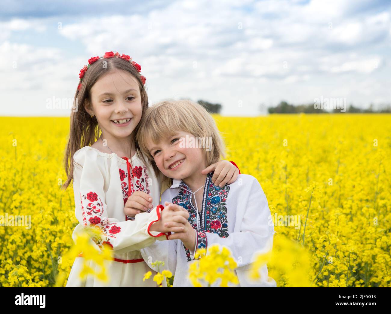 Felice ragazzo e ragazza di 6-7 anni in maglia nazionale ucraino stand abbracciare tra fioritura giallo campo di colza. Giorno di indipendenza. CHIL Foto Stock