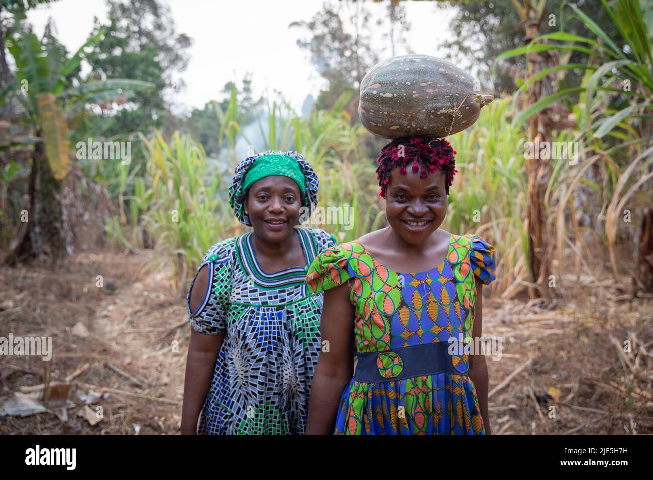 Due contadine nei campi vestiti con abiti tradizionali africani hanno appena raccolto una zucca, donne e lavoro in africa Foto Stock