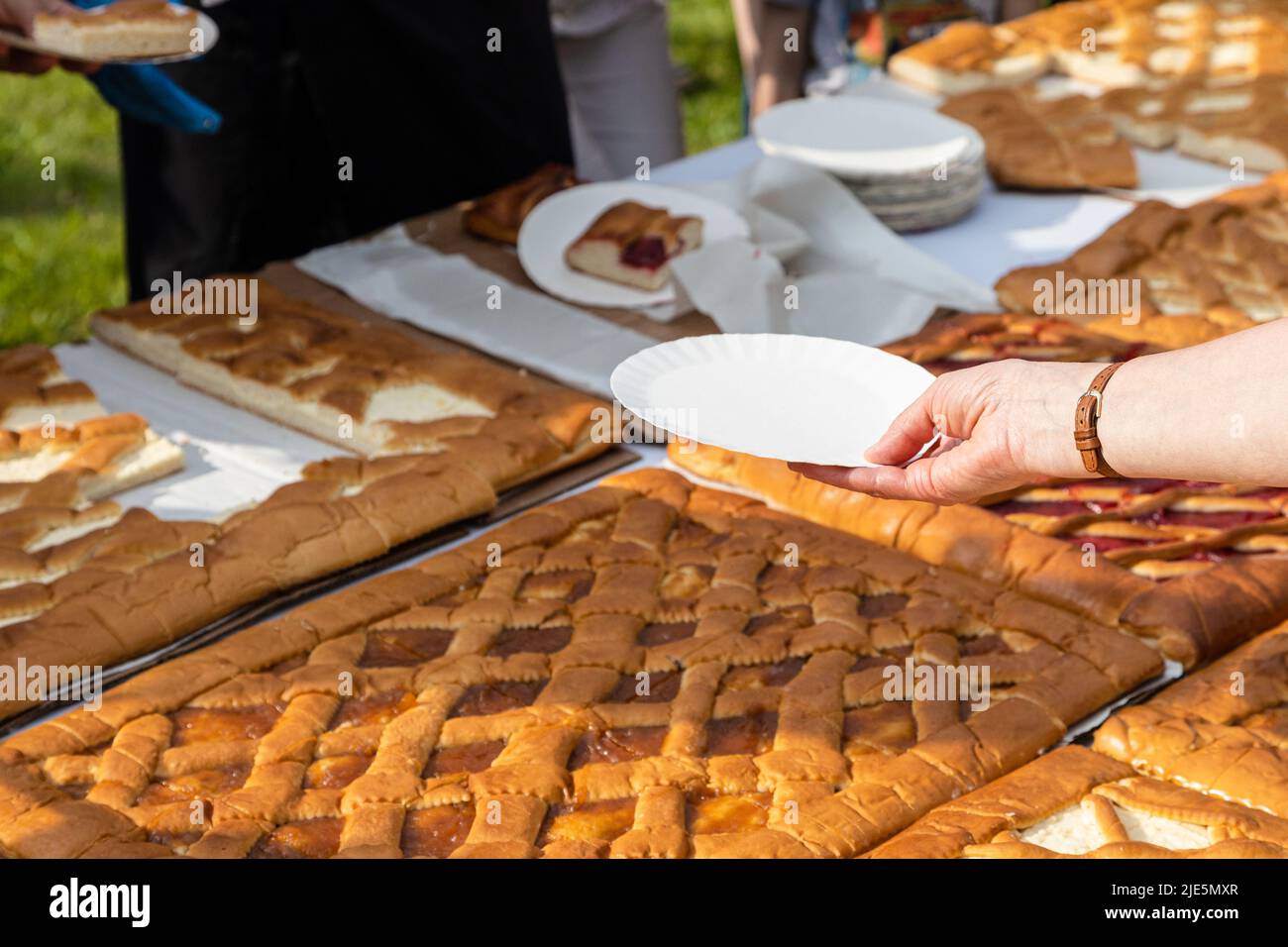 la mano con il piatto di carta vuoto raggiunge per una porzione di torta dolce aperta Foto Stock