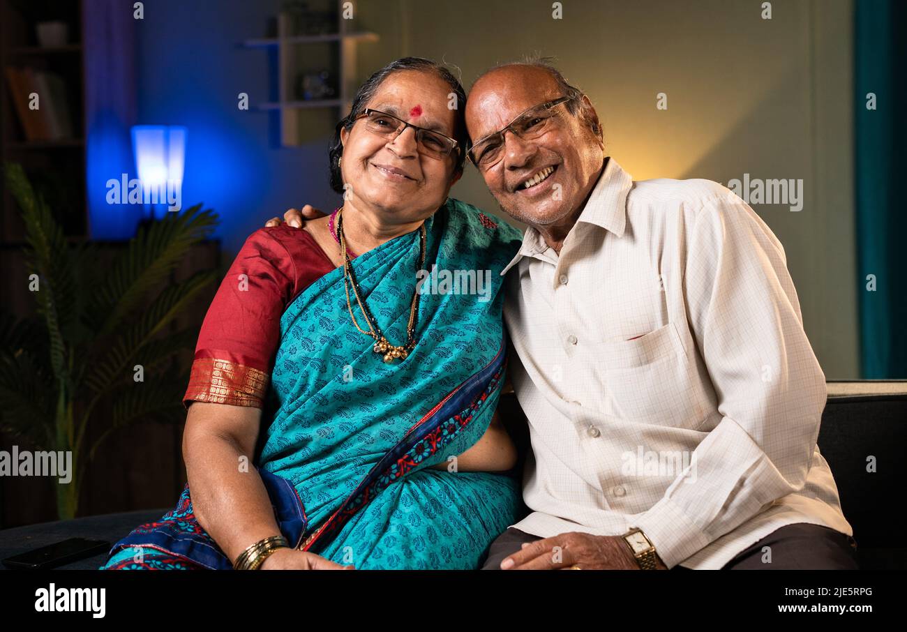 Ritratto girato di coppia anziana felice abbracciandosi a vicenda guardando macchina fotografica a casa- concetto di rapporto, felicità e legame di famiglia Foto Stock