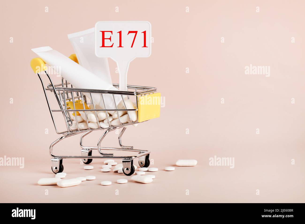 Diossido di titanio, E171, additivo pericoloso concetto. Gomma, pillole, dentifricio, crema in cestino e segno con E171 su sfondo beige. Spazio copia Foto Stock