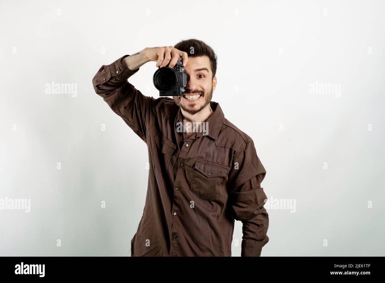 Uomo allegro casual che indossa abiti casual in posa isolata su sfondo bianco per scattare foto con la fotocamera dslr. Fotografo che copre il suo volto con Foto Stock
