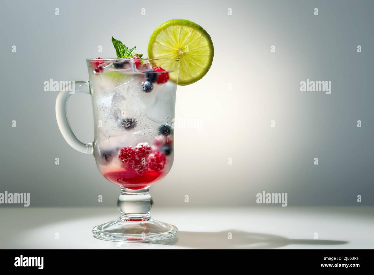 Rinfrescante cocktail estivo con ghiaccio, lime e frutti di bosco in un bicchiere, copyspace. Foto Stock