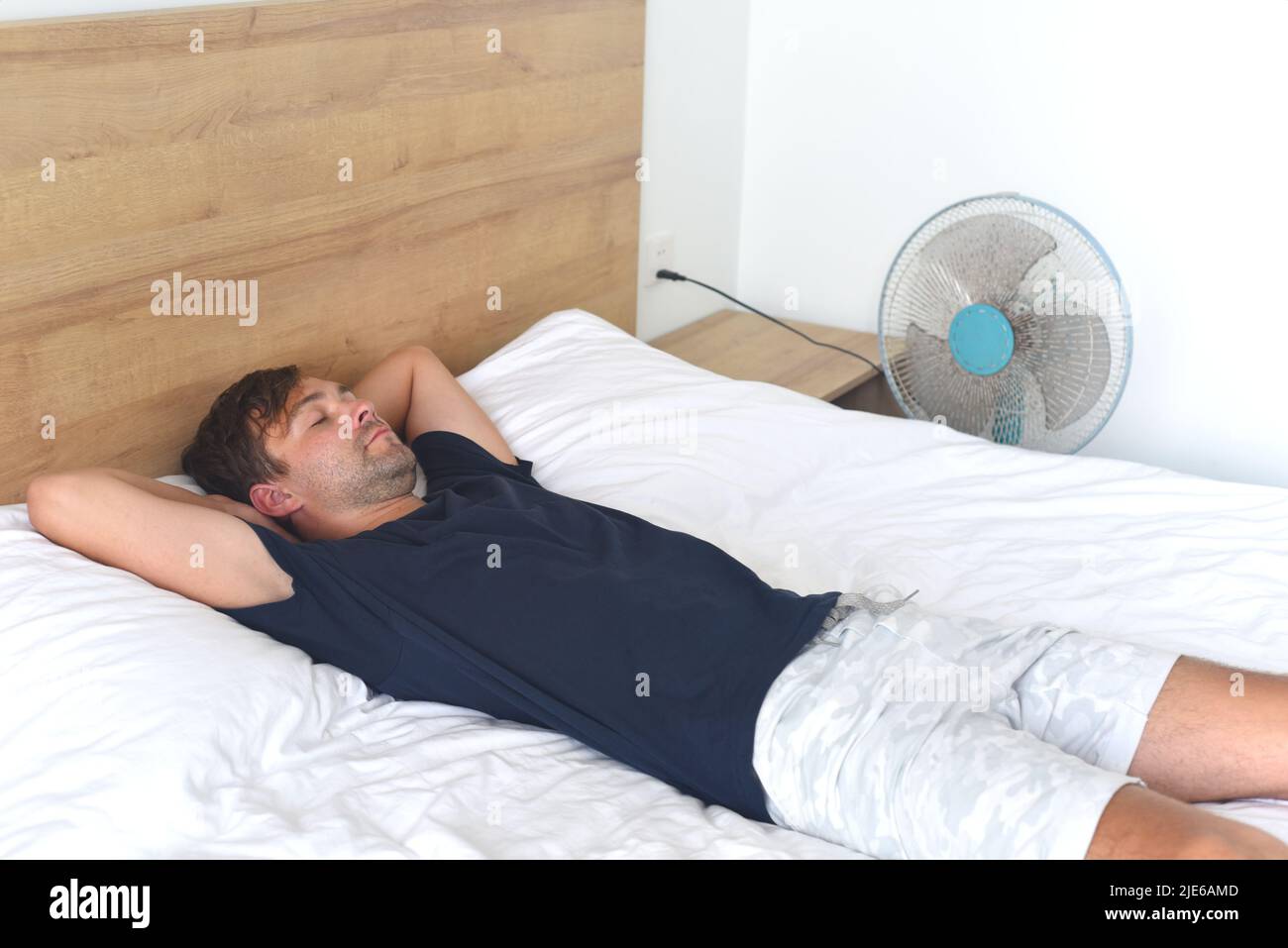 Giovane uomo che si stende e dorme contro il ventilatore in una calda giornata estiva Foto Stock