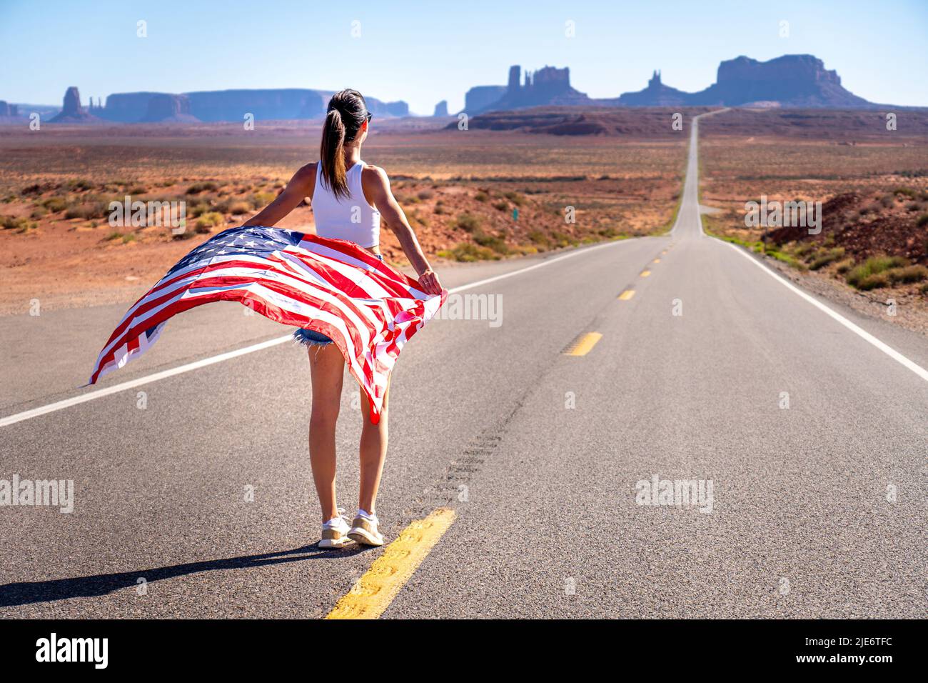 Ragazza bruna sconosciuta da dietro in Monument Valley tenendo una bandiera degli Stati Uniti d'America, indossando jeans corti e una cima bianca del carro armato Foto Stock