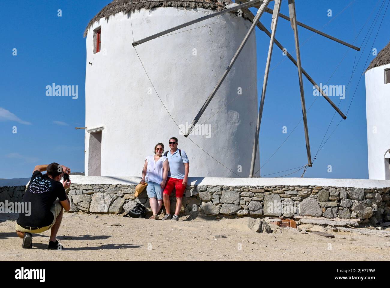 Mykonos, Grecia - Giugno 2022: Persone che posano per una fotografia di fronte a uno dei famosi mulini a vento sull'isola greca di Mykonos Foto Stock