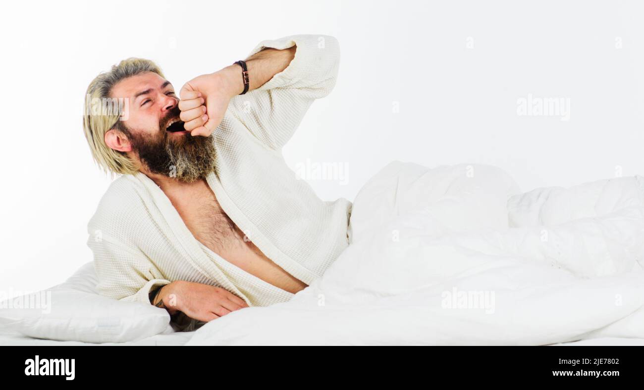 Bell'uomo bearded al mattino sbadigliando e stretching a letto. Ragazzo addormentato in accappatoio. Risveglio. Foto Stock
