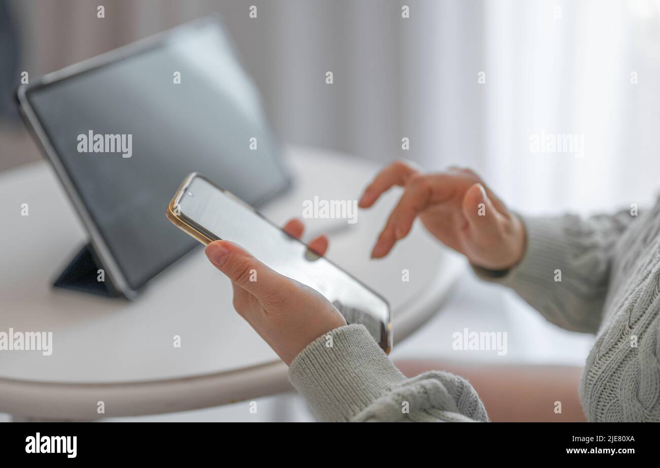 donna che lavora da casa con tablet e telefono. Donna mani con cellulare. Vista ripresa ritagliata delle mani donna che tengono il telefono cellulare con i contatti. Utilizzo Foto Stock