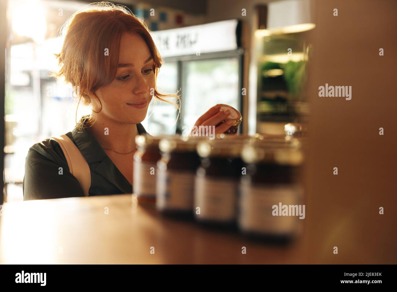 Giovane donna felice che legge l'etichetta di un prodotto alimentare nella sezione di cibo bruta di un negozio di alimentari. Allegro giovane donna drogheria shopping in un trendy Foto Stock