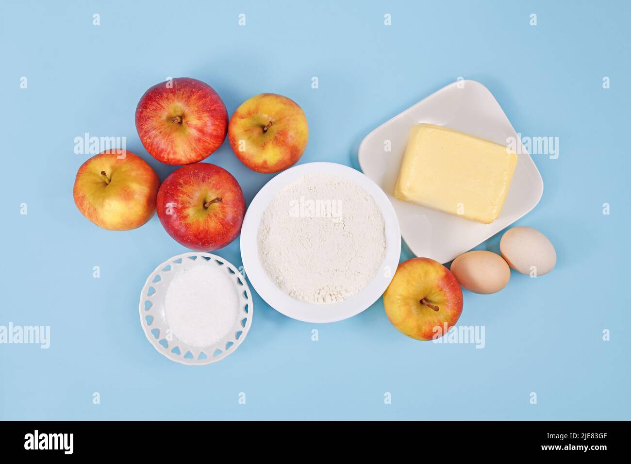 Ingredienti per la cottura a torta di mele con burro, farina, zucchero, uova e frutta su sfondo blu Foto Stock