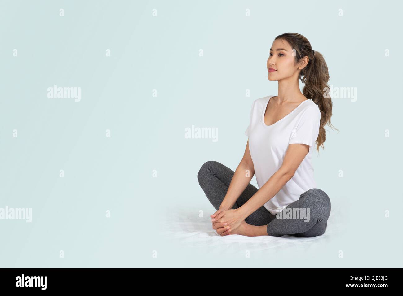 Foto isolata di una donna seduta sul pavimento che fa tratti o yoga per un concetto sano. Foto Stock